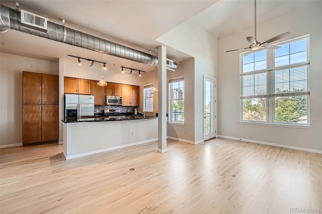 kitchen with brown cabinets, stainless steel appliances, dark countertops, visible vents, and open floor plan