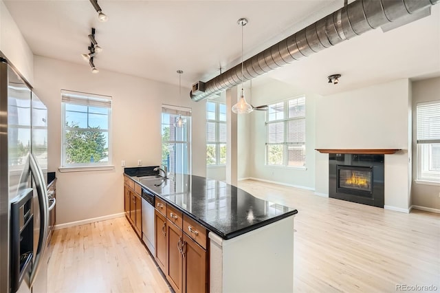 kitchen featuring brown cabinets, decorative light fixtures, appliances with stainless steel finishes, a glass covered fireplace, and light wood-type flooring