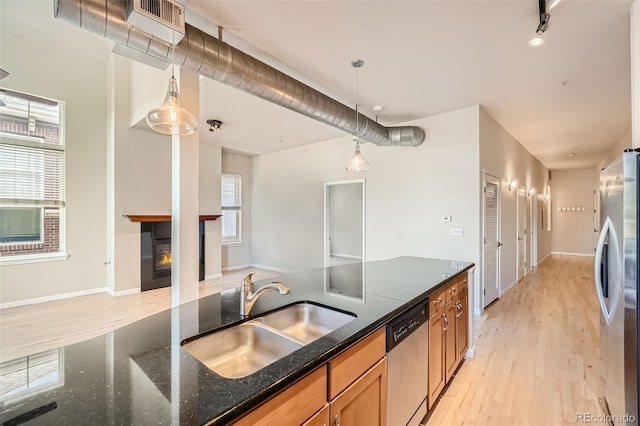 kitchen featuring stainless steel appliances, a sink, hanging light fixtures, dark stone counters, and brown cabinetry