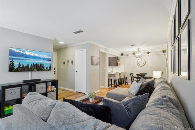 living room with ornamental molding, baseboards, visible vents, and light wood-type flooring