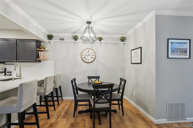 dining space featuring visible vents, baseboards, ornamental molding, an inviting chandelier, and light wood-style floors