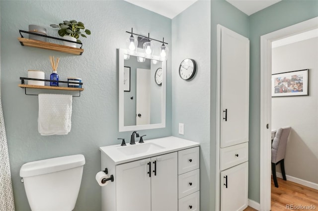 bathroom featuring baseboards, toilet, wood finished floors, and vanity