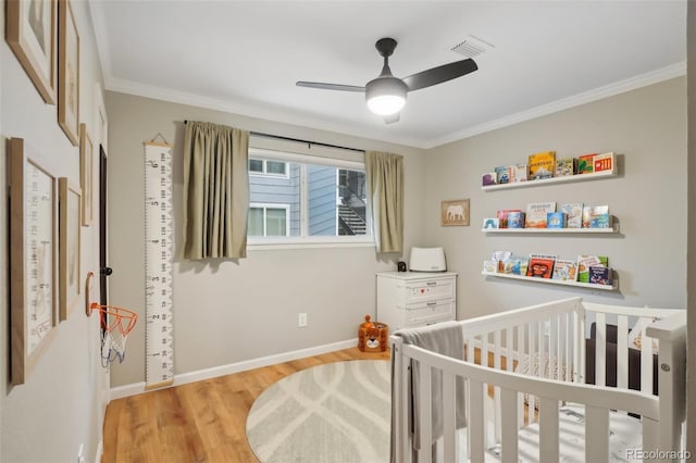 bedroom with wood finished floors, visible vents, baseboards, ornamental molding, and a crib