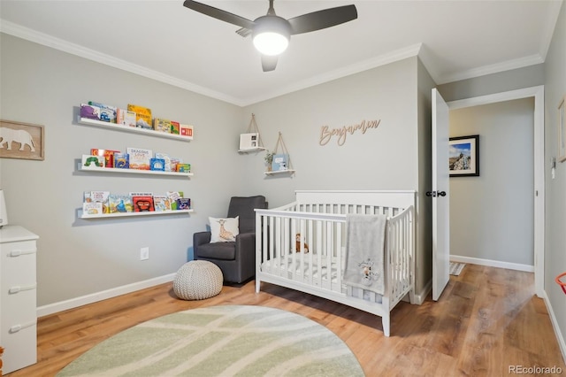 bedroom with baseboards, a nursery area, wood finished floors, and crown molding