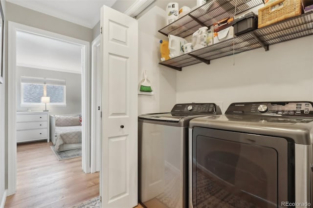 clothes washing area featuring laundry area, washing machine and dryer, light wood-style flooring, and ornamental molding