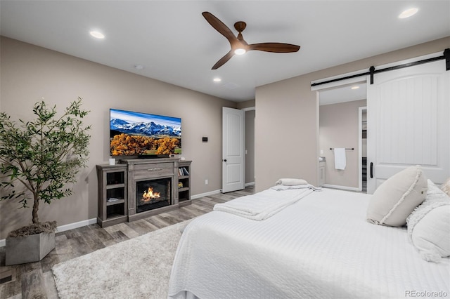 3059 Morningbird Ln, Castle Rock, CO 80109 - bedroom with wood finished floors, a barn door, recessed lighting, a glass covered fireplace, and baseboards