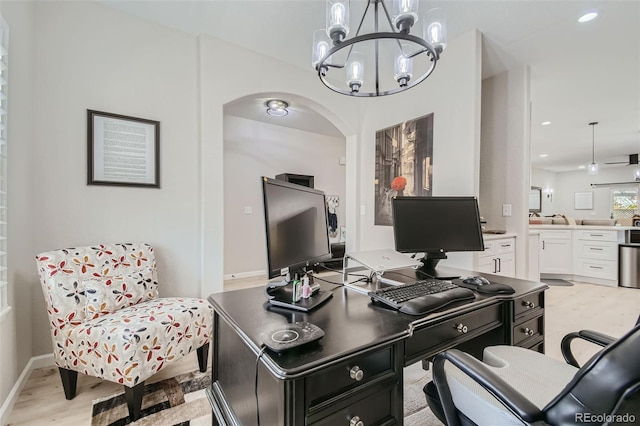 home office featuring ceiling fan with notable chandelier and light hardwood / wood-style flooring