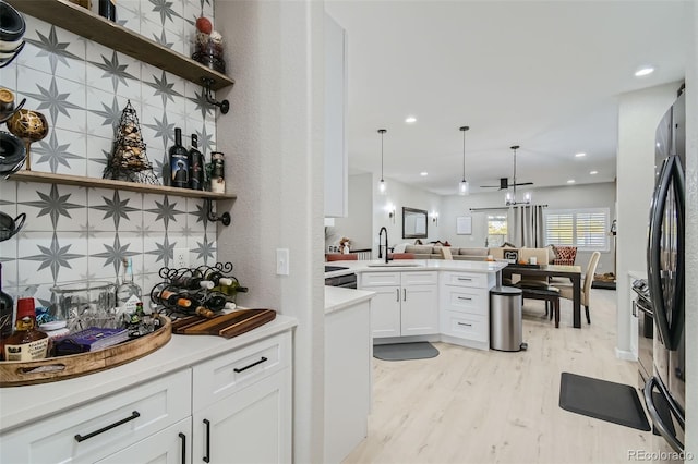 kitchen featuring white cabinetry, sink, hanging light fixtures, black fridge, and light hardwood / wood-style flooring