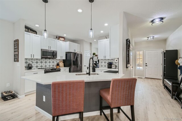 kitchen with hanging light fixtures, sink, stainless steel appliances, and light hardwood / wood-style flooring