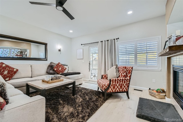 living room featuring a tile fireplace, a wealth of natural light, ceiling fan, and light hardwood / wood-style floors