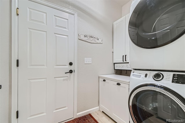 clothes washing area featuring light hardwood / wood-style floors, cabinets, and stacked washing maching and dryer