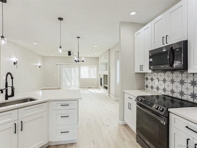 kitchen featuring black stove, decorative light fixtures, white cabinetry, and sink