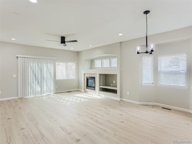 unfurnished living room featuring a tile fireplace, light hardwood / wood-style flooring, and ceiling fan with notable chandelier