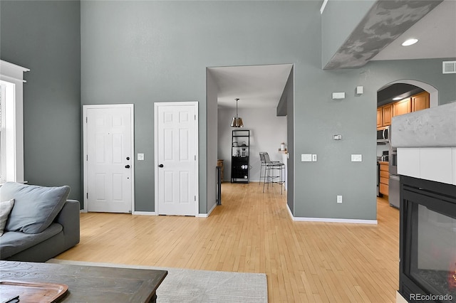 living area with arched walkways, a high ceiling, light wood-type flooring, and baseboards