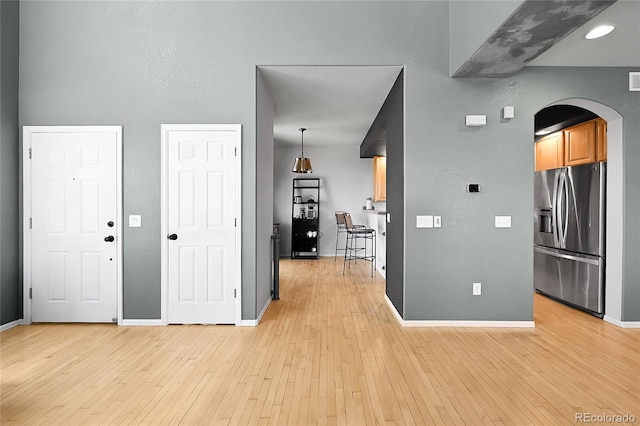 entryway with arched walkways, light wood-style floors, and baseboards