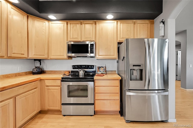 kitchen with stainless steel appliances, light brown cabinetry, light wood finished floors, and tile counters