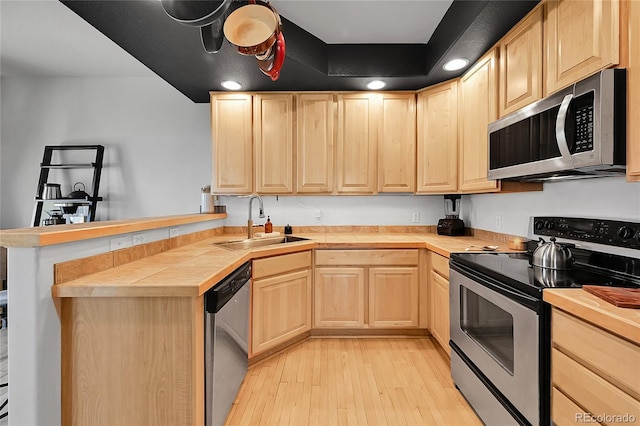 kitchen featuring stainless steel appliances, light brown cabinetry, a sink, and a peninsula