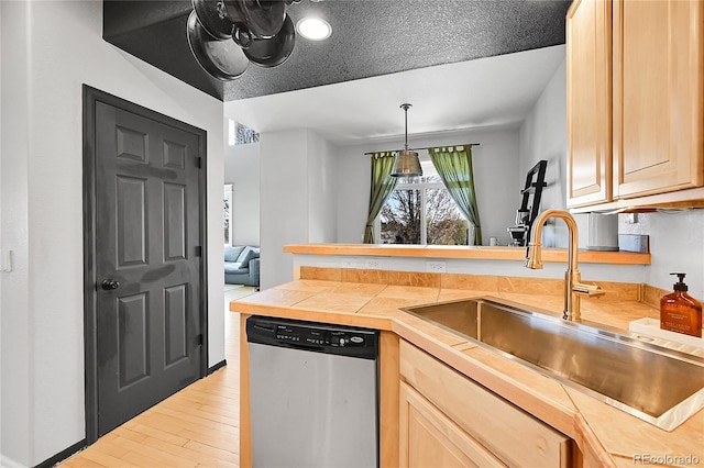 kitchen with stainless steel dishwasher, a sink, a peninsula, light wood-style flooring, and light brown cabinetry