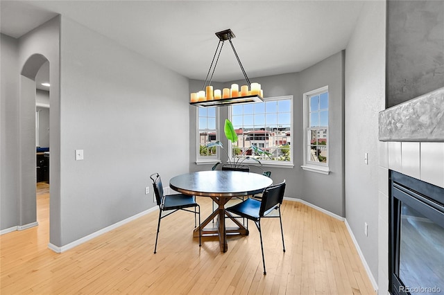 dining area with arched walkways, light wood-style flooring, a tiled fireplace, and baseboards