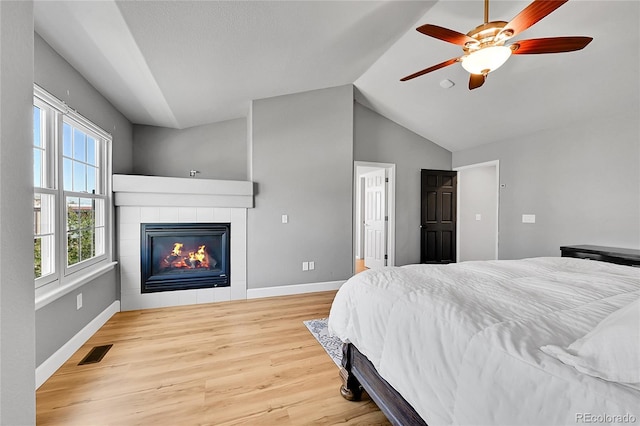 bedroom featuring wood finished floors, vaulted ceiling, a tiled fireplace, baseboards, and a ceiling fan