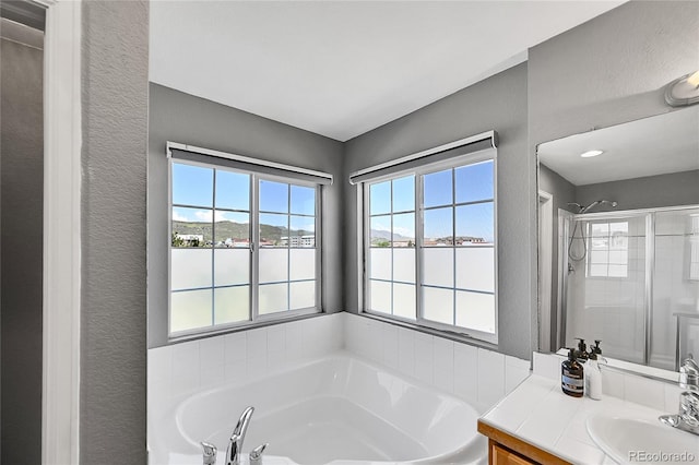 bathroom with healthy amount of natural light, a garden tub, vanity, a textured wall, and a shower