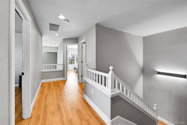 hallway featuring an upstairs landing, light wood finished floors, baseboards, and recessed lighting