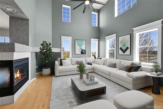 living room featuring a towering ceiling, ceiling fan, a glass covered fireplace, and wood finished floors