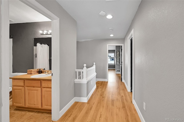 corridor with a sink, light wood-type flooring, baseboards, and recessed lighting