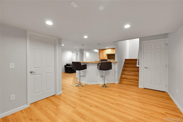 kitchen featuring light wood finished floors, baseboards, a breakfast bar area, a peninsula, and recessed lighting