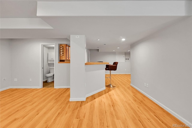 kitchen with baseboards, light wood-type flooring, recessed lighting, a peninsula, and a breakfast bar