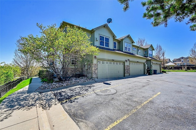 view of front facade with a garage, fence, a residential view, and stone siding
