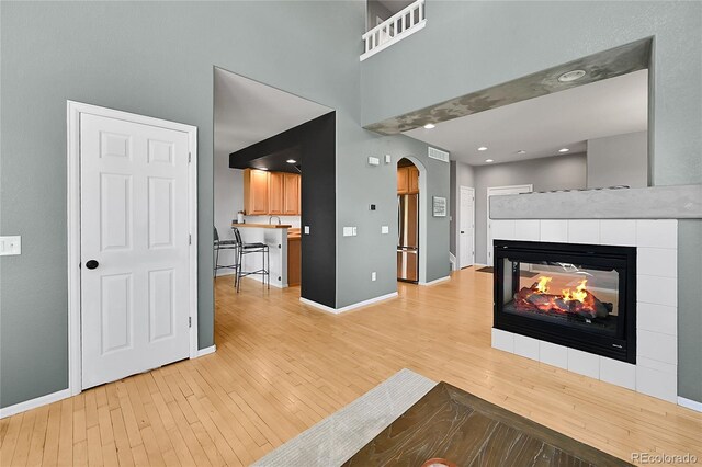 5906 S Youngfield Way, Littleton, CO 80127 - unfurnished living room featuring light wood-style floors, arched walkways, a tiled fireplace, and a towering ceiling