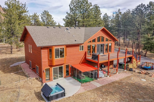 rear view of property with a hot tub, a deck, and a patio