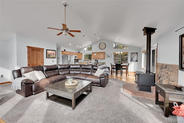 living room featuring light carpet, ceiling fan with notable chandelier, high vaulted ceiling, and a wood stove