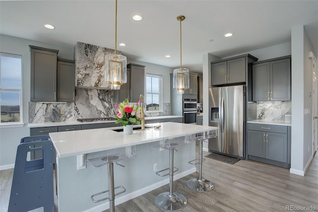 kitchen with light countertops, light wood-style flooring, a kitchen island with sink, and appliances with stainless steel finishes
