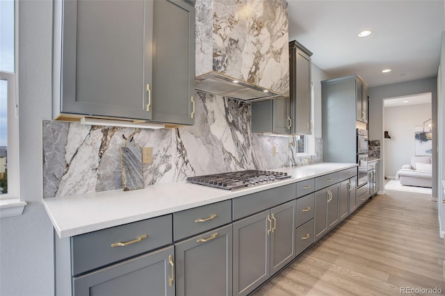 kitchen with gray cabinetry, stainless steel gas cooktop, wall chimney range hood, and light wood-type flooring