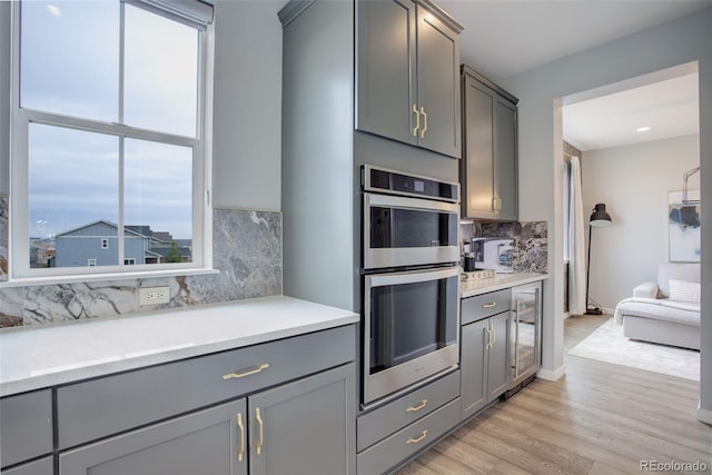 kitchen with light wood finished floors, gray cabinets, light countertops, and stainless steel double oven