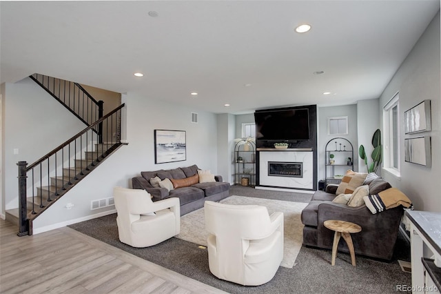 living area with stairs, recessed lighting, visible vents, a high end fireplace, and wood finished floors