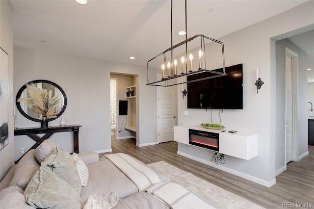 living room with baseboards, wood finished floors, a glass covered fireplace, and a notable chandelier