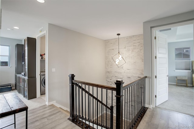 corridor featuring an upstairs landing, visible vents, baseboards, light wood-type flooring, and washer / dryer