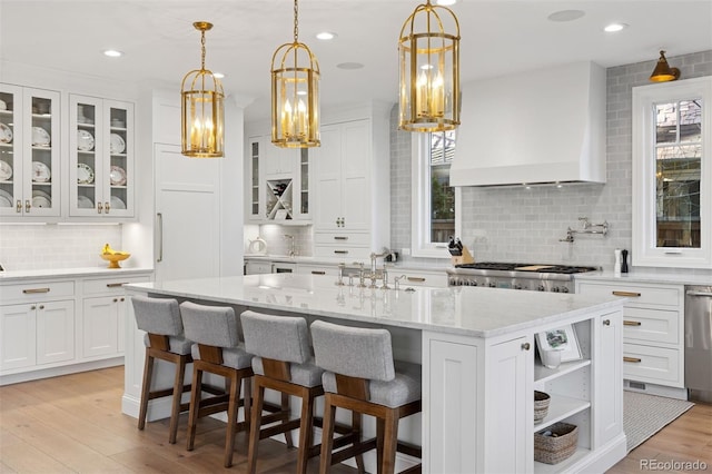 2130 S Milwaukee St, Denver, CO 80210 - kitchen featuring light stone countertops, custom exhaust hood, a kitchen island with sink, white cabinetry, and light wood-type flooring