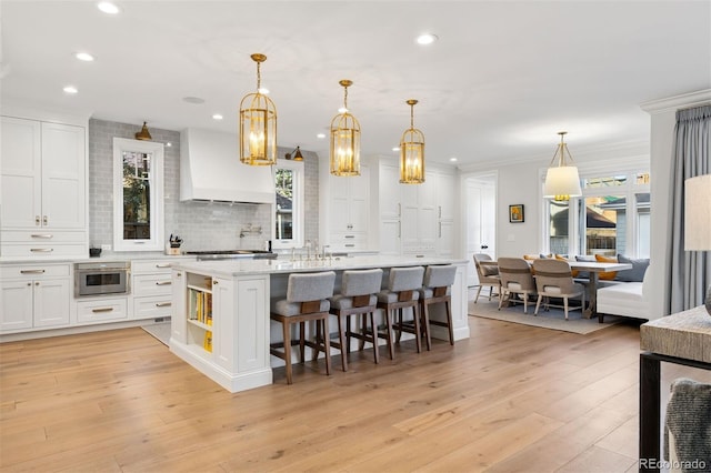 2130 S Milwaukee St, Denver, CO 80210 - kitchen with custom exhaust hood, white cabinets, tasteful backsplash, and light wood-style flooring