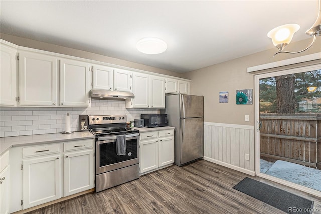 kitchen with wainscoting, stainless steel appliances, light countertops, under cabinet range hood, and white cabinetry