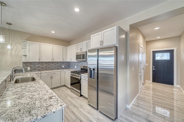 kitchen with sink, decorative light fixtures, light stone counters, white cabinetry, and stainless steel appliances