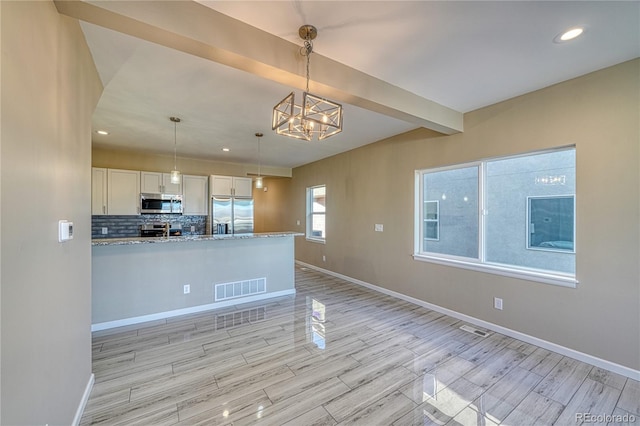 kitchen with light stone countertops, white cabinetry, stainless steel appliances, pendant lighting, and light hardwood / wood-style floors