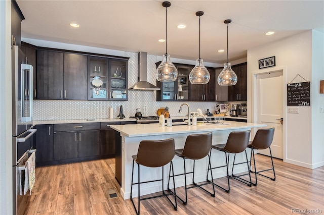 11253 Moondance Trl, Littleton, CO 80125 - kitchen featuring wall chimney range hood, light countertops, light wood finished floors, backsplash, and a kitchen breakfast bar