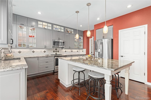 kitchen with sink, gray cabinetry, stainless steel appliances, light stone counters, and a kitchen island