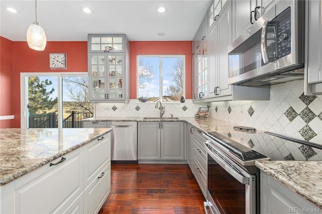 kitchen with pendant lighting, sink, appliances with stainless steel finishes, light stone counters, and dark hardwood / wood-style flooring