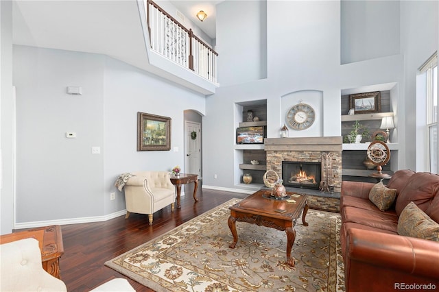 living room with a towering ceiling, dark hardwood / wood-style floors, a fireplace, plenty of natural light, and built in shelves