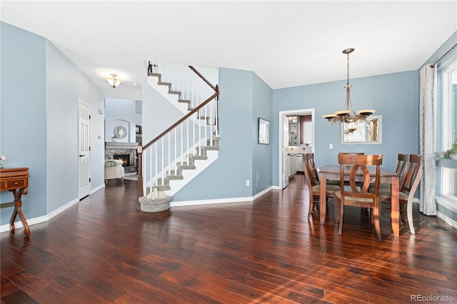 dining area featuring dark hardwood / wood-style floors, a chandelier, and a stone fireplace